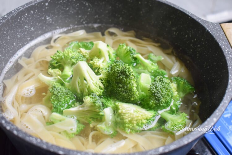 Fresh broccoli florets added to boiling fettuccine pasta in a large pot
