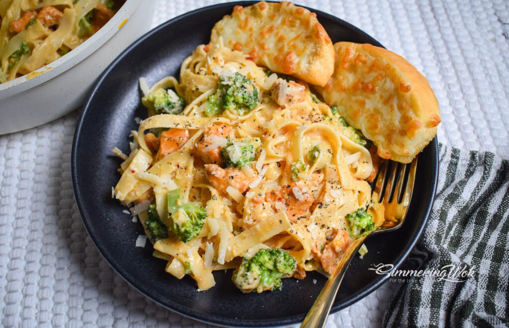 Butter garlic chicken and broccoli fettuccine hero shot served on a dark plate with garlic bread and a gold fork