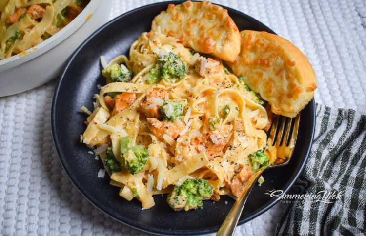Butter garlic chicken and broccoli fettuccine hero shot served on a dark plate with garlic bread and a gold fork