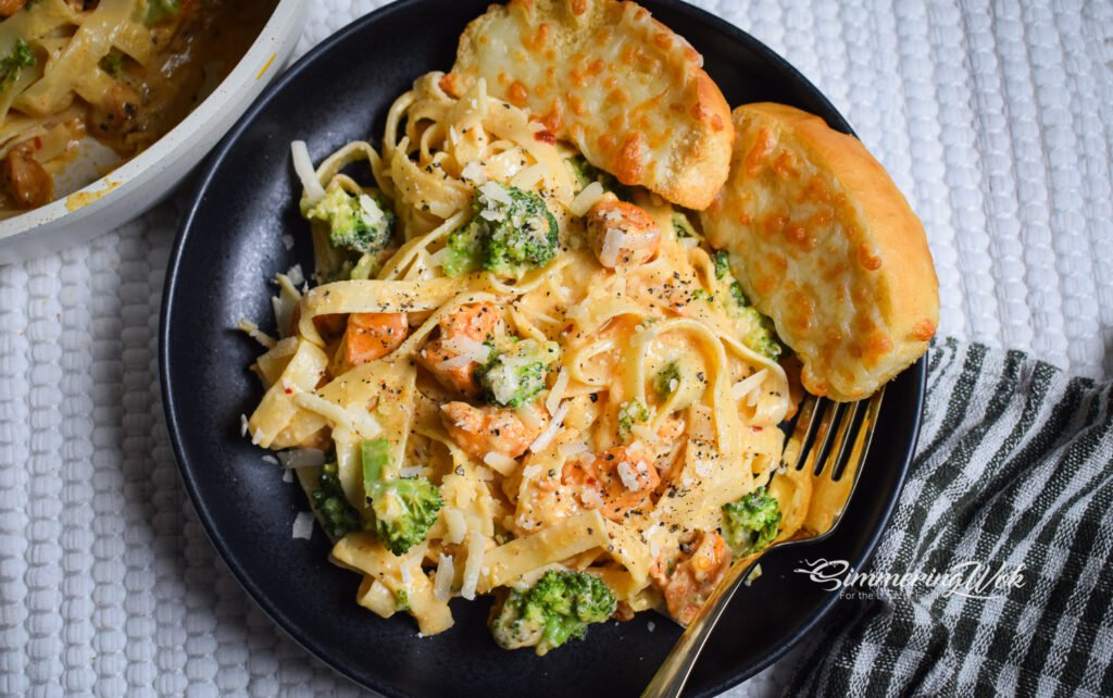 Butter garlic chicken broccoli fettuccine served on a dark plate with garlic bread tucked alongside