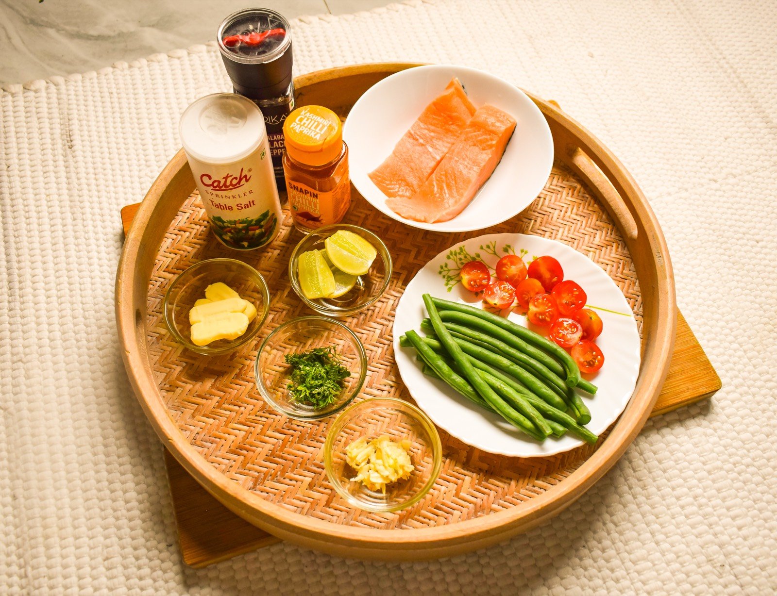 Flat lay of all ingredients for butter garlic salmon recipe including salmon fillets, garlic, butter, lime, cilantro, salt, paprika, green beans and cherry tomatoes