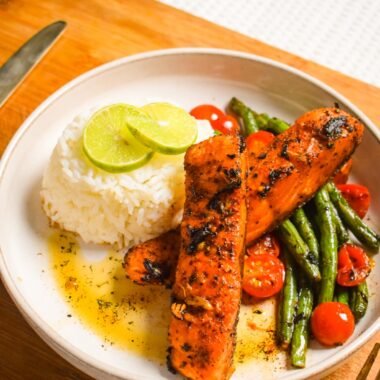 Butter garlic salmon with cilantro served with jasmine rice, sauteed green beans and cherry tomatoes on a white plate