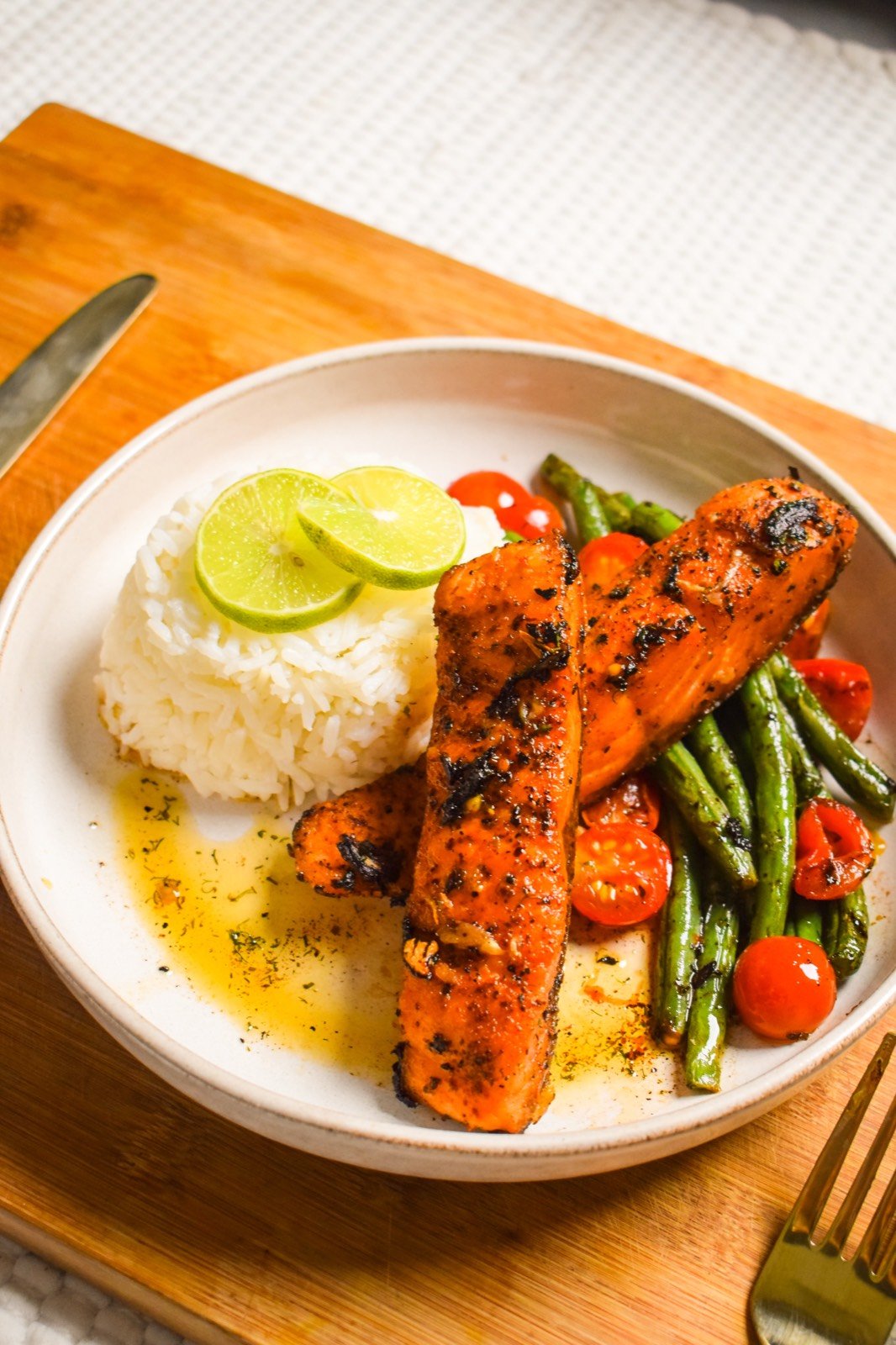 Butter garlic salmon with cilantro served with jasmine rice, sauteed green beans and cherry tomatoes on a white plate