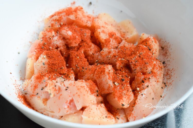 Chicken cubes seasoned with paprika and garlic powder in a white bowl showing vivid orange-red color