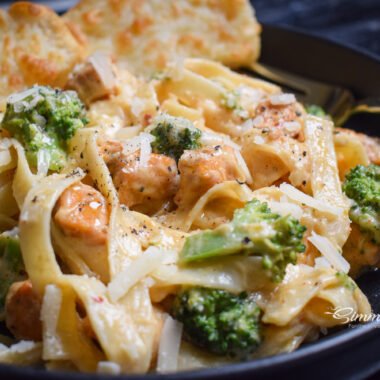 Creamy chicken broccoli fettuccine with garlic bread on a dark plate overhead view