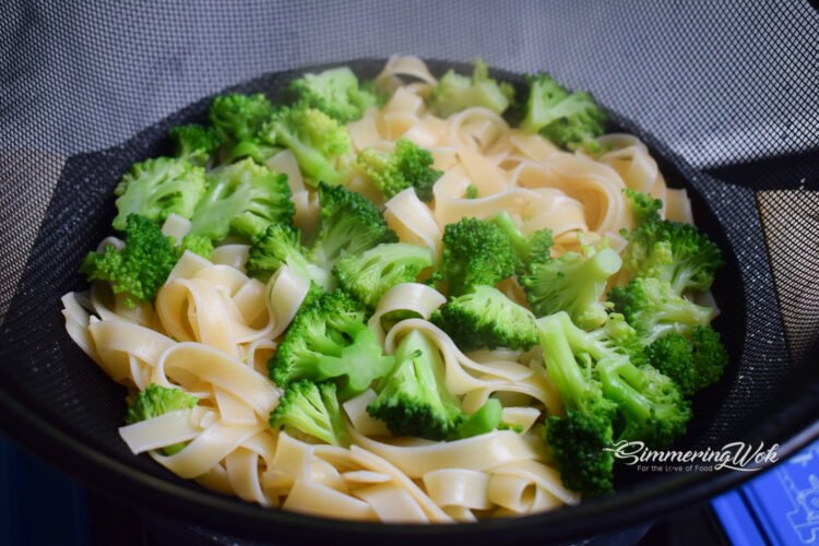 Drained fettuccine pasta and bright green broccoli florets in a strainer