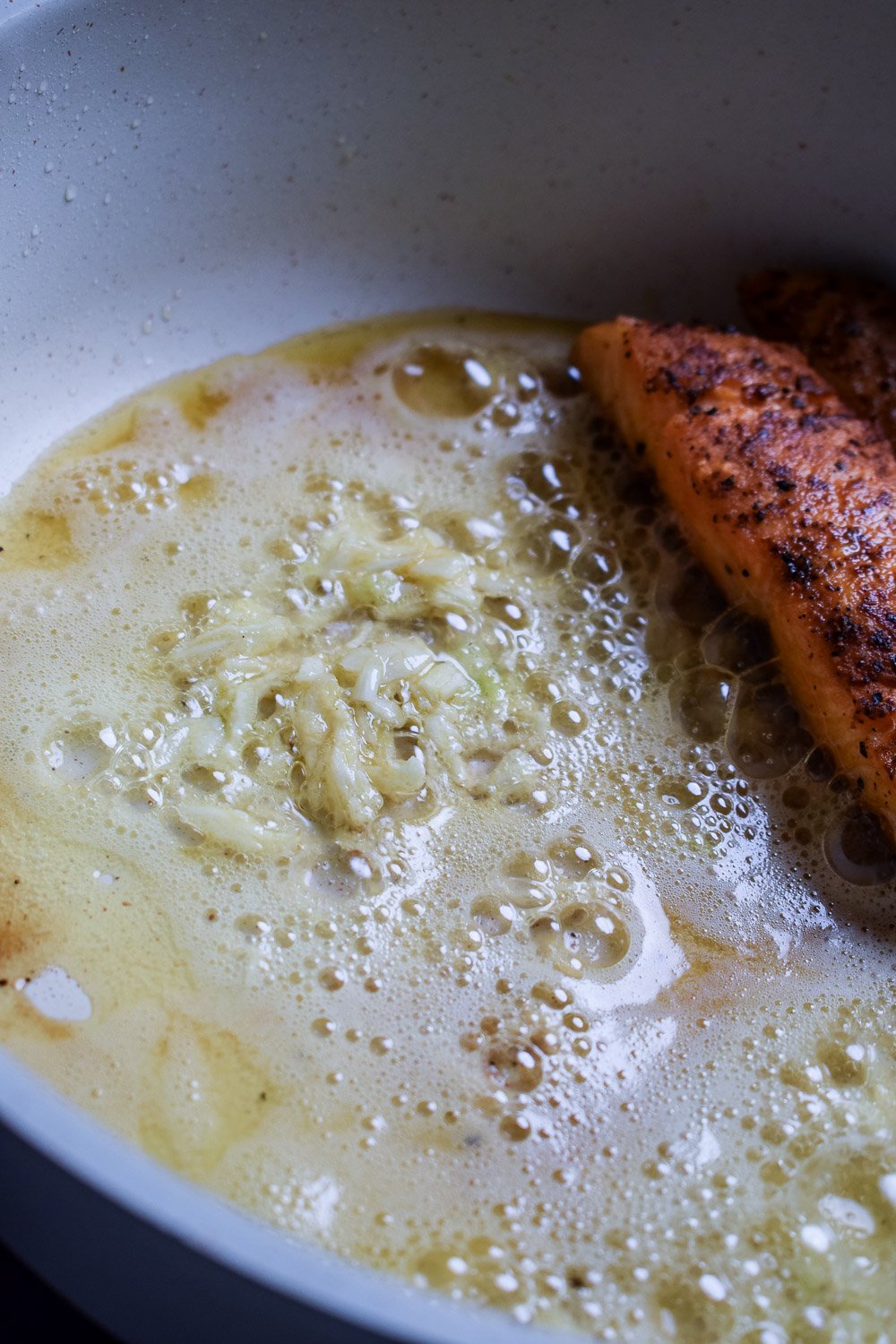 Minced garlic sizzling in foaming butter next to salmon fillet