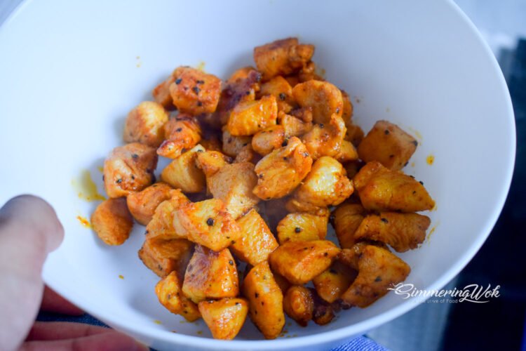 Golden cooked chicken cubes set aside in a white bowl