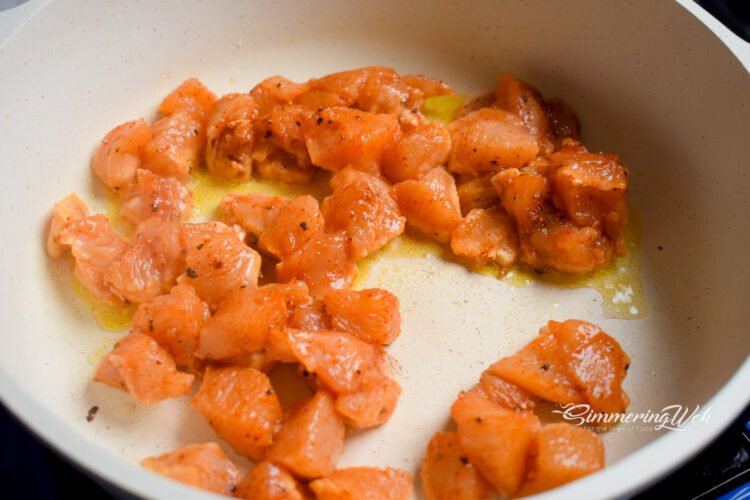 Seasoned chicken cubes placed into a hot pan with olive oil beginning to sear