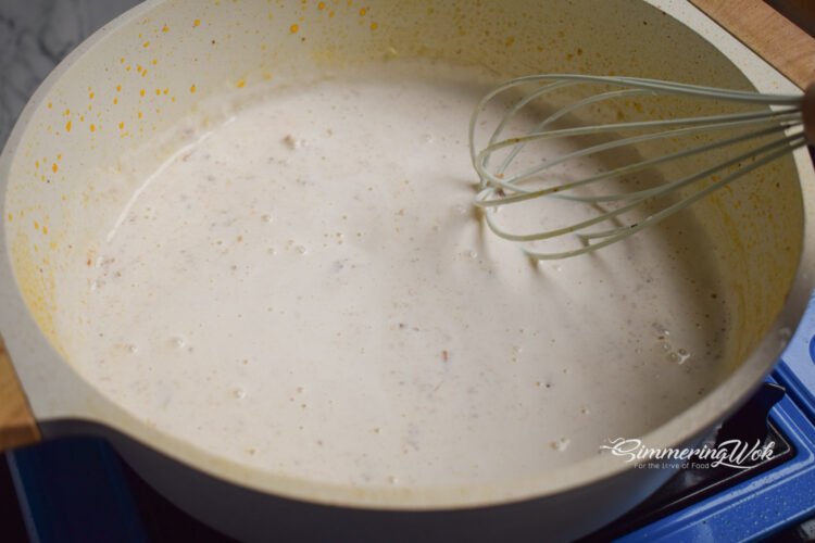 Whisking half and half cream into the garlic butter roux to create a smooth creamy sauce